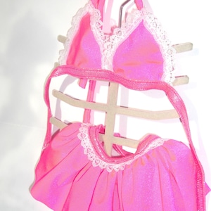 May include: Pink sparkly bikini top and skirt with white lace trim. The top has a halter style and the skirt is a mini skirt.
