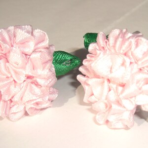 May include: Two pink fabric flower hair clips with green leaves.