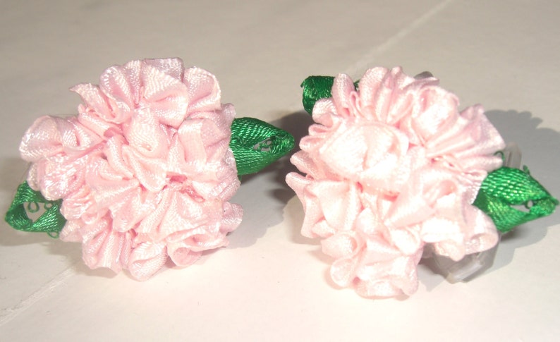 May include: Two pink fabric flower hair clips with green leaves.