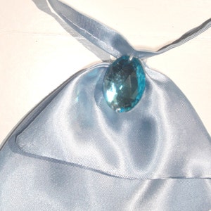 May include: A light blue satin fabric pouch with a large, clear, light blue gemstone pendant.