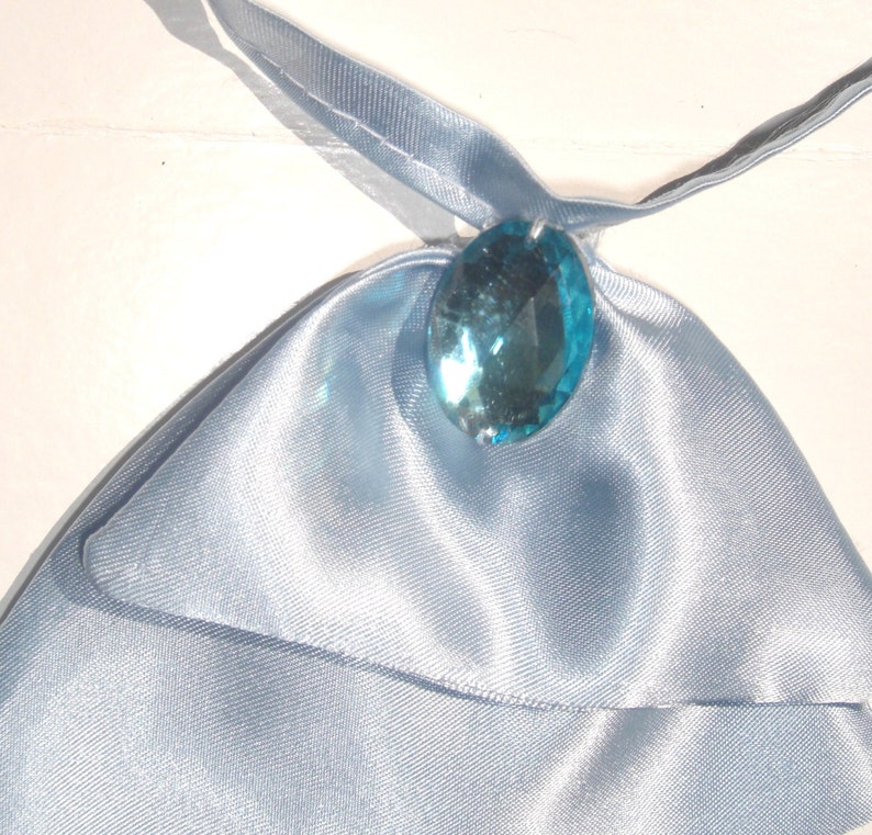 May include: A light blue satin fabric pouch with a large, clear, light blue gemstone pendant.