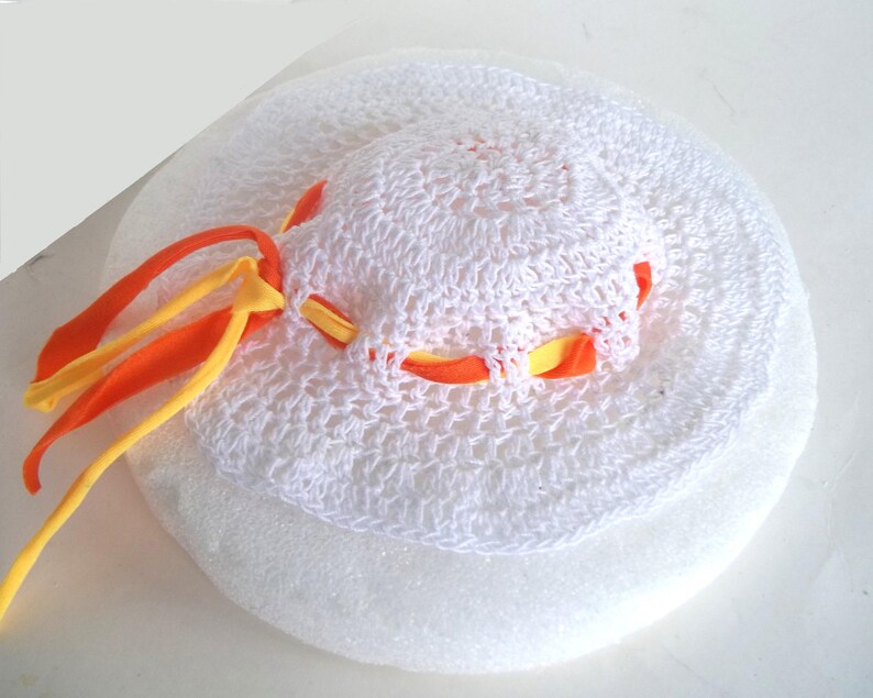 May include: White crocheted sun hat with orange and yellow ribbon trim.