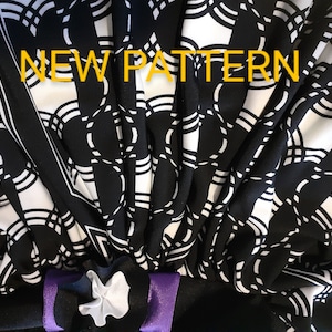 May include: Black and white fabric with a geometric pattern of circles and lines. The fabric is folded and has a purple ribbon tied around it. The text "NEW PATTERN" is written in yellow across the top of the image.