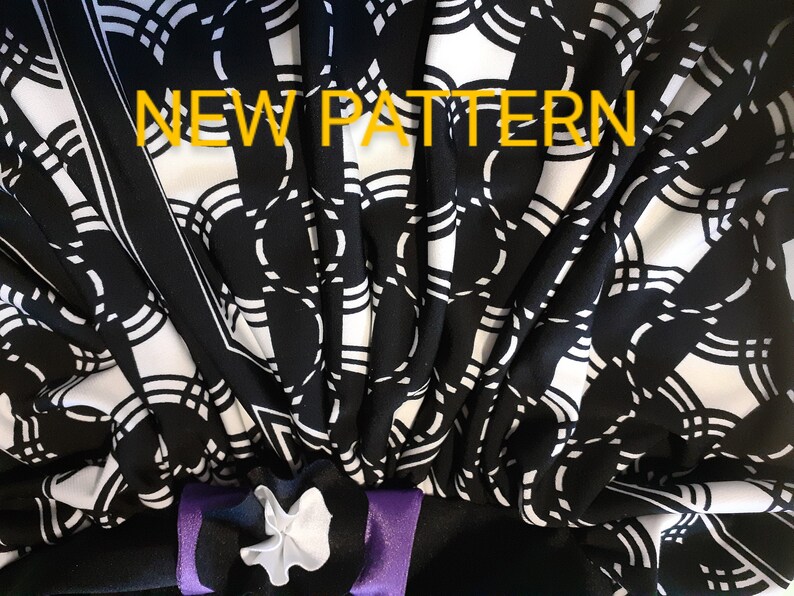 May include: Black and white fabric with a geometric pattern of circles and lines. The fabric is folded and has a purple ribbon tied around it. The text "NEW PATTERN" is written in yellow across the top of the image.