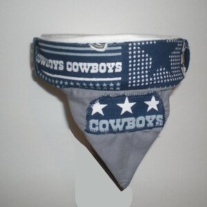 May include: A grey and blue fabric dog bandana with the words "COWBOYS" printed on it. The bandana has three white stars and a white and blue patterned border.