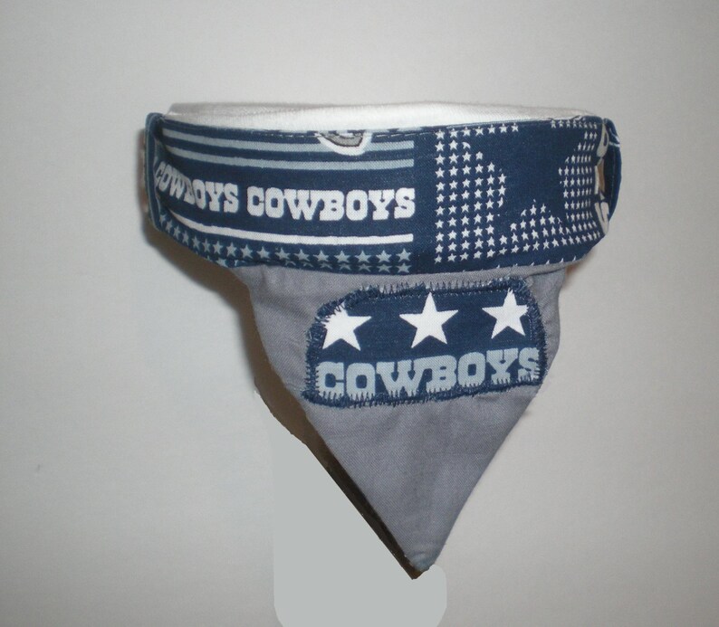 May include: A grey and blue fabric dog bandana with the words "COWBOYS" printed on it. The bandana has three white stars and a white and blue patterned border.