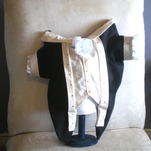 Puede incluir: Una chaqueta formal negra y crema con botones dorados. La chaqueta tiene solapas y pu&ntilde;os de sat&eacute;n color crema y un lazo blanco. La chaqueta se exhibe en una cabeza de maniqu&iacute;.
