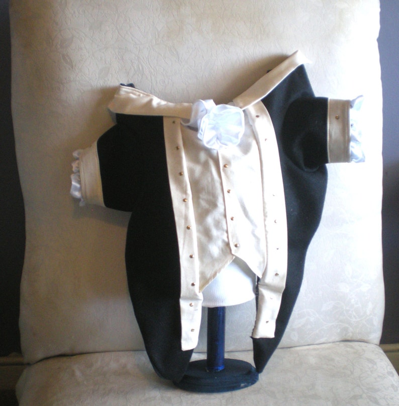 Puede incluir: Una chaqueta formal negra y crema con botones dorados. La chaqueta tiene solapas y pu&ntilde;os de sat&eacute;n color crema y un lazo blanco. La chaqueta se exhibe en una cabeza de maniqu&iacute;.