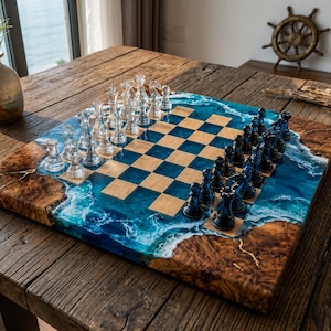 May include: A square chessboard featuring a central grid of light wood squares alternating with translucent blue resin squares. The board edges are made of natural burl wood with a wavy blue and white resin ocean design. Clear and dark blue chess pieces.