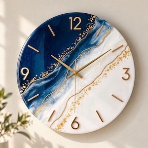 May include: A round wall clock featuring a swirling design of deep navy blue and white resin with gold leaf accents. The clock face includes gold-colored numerals at the 12, 3, 6, and 9 positions, with thin gold hands and simple gold markers.