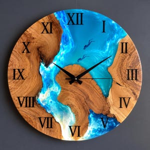 Könnte beinhalten: Eine runde Wanduhr mit einem Zifferblatt aus Naturholz und einer zentralen Einlage aus durchscheinendem blauem Harz, die an einen Fluss erinnert. Das Design zeigt zwei kleine Taucher-Silhouetten im blauen Bereich und schwarze römische Ziffern.