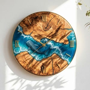 May include: A round wall clock featuring a natural wood grain face with a central river-like inlay of blue resin depicting ocean waves and a whale shark. The clock has gold-colored hands and gold Roman numeral markers at the twelve, three, six, and nine positions.