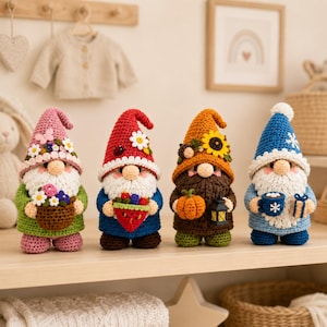 May include: Four crocheted gnome figurines standing in a row. The first wears a pink hat with flowers and holds a basket of flowers. The second has a red hat with a ladybug and holds a strawberry. The third has an orange hat with a sunflower and holds a pumpkin and lantern. The fourth wears a blue hat with a snowflake and holds a mug and gift.