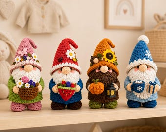 May include: Four crocheted gnome figurines standing in a row. The first wears a pink hat with flowers and holds a basket of flowers. The second has a red hat with a ladybug and holds a strawberry. The third has an orange hat with a sunflower and holds a pumpkin and lantern. The fourth wears a blue hat with a snowflake and holds a mug and gift.
