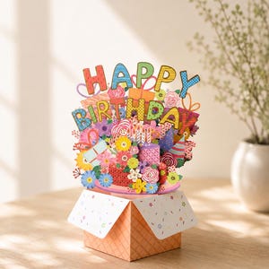 May include: A vibrant pop-up birthday card with the words "Happy Birthday". The card is filled with flowers, gifts, and candles, emerging from a decorative box. The card is set on a wooden surface. The card is a cheerful celebration.