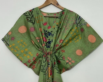 May include: A light green kaftan featuring a V-neckline and a drawstring waist. The garment is decorated with a colorful botanical print including orange sun-like circles, yellow floral clusters, pink blossoms, and dark green foliage patterns.