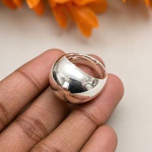May include: A polished silver ring with a rounded, dome-like design. The ring reflects light, creating a bright, shiny appearance. The jewellery is a simple, yet elegant accessory.
