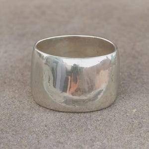 May include: A wide, polished silver band ring with a smooth, reflective surface. The ring features a thick, continuous metal construction with a rounded profile, showcasing a bright, metallic finish that captures light across its curved exterior.