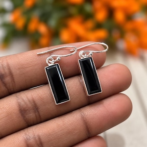 May include: A pair of silver drop earrings featuring rectangular black onyx stones set in polished silver frames. Each earring hangs from a simple silver hook wire, showcasing a sleek, elongated geometric design with a smooth, reflective surface.