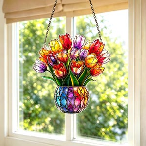 May include: A stained glass window hanging featuring a bouquet of colorful tulips in a vase. The tulips are red, yellow, orange, and purple. The vase is a mosaic of rainbow colors, suspended by a chain.