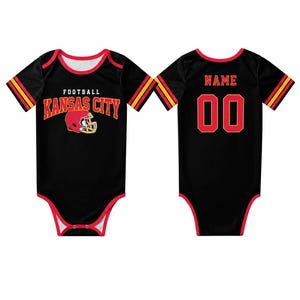 May include: Black baby bodysuit with red and yellow accents. The front features the text "FOOTBALL KANSAS CITY" with a football helmet graphic. The back has the word "NAME" above the number "00".