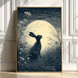 May include: A framed art print depicting a black hare in a field, looking up at a large, pale yellow moon. The artwork is in monochrome, with detailed illustrations of grass and wildflowers, creating a serene night scene.