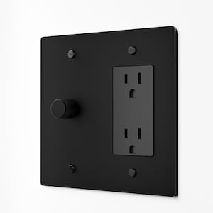 May include: A matte black wall plate featuring a circular knurled dimmer knob on the left and a standard two-slot electrical outlet on the right. The square plate is secured to the wall with four matching black screws at the corners.