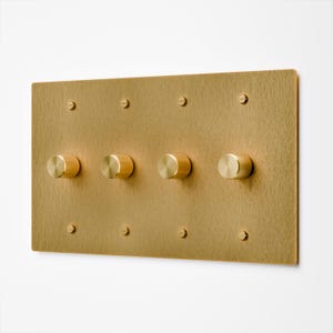 May include: A rectangular, brushed brass light switch plate with four round, ridged dimmer knobs. The plate is secured with eight small screws. The design is minimalist and modern.