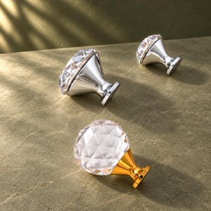 May include: Three cabinet knobs with faceted clear glass tops shaped like diamonds. Two knobs feature polished silver-tone metal bases, while one knob has a bright gold-tone metal base. Each knob has a circular mounting plate at the bottom.