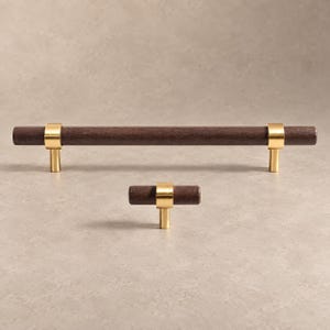 May include: A long cylindrical dark brown wooden cabinet pull and a matching smaller T-shaped wooden knob, both featuring polished gold-tone metal accents that secure the wood to the mounting posts for a clean and functional hardware design.