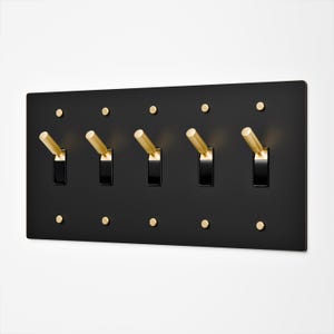 May include: A rectangular matte black wall plate featuring five toggle light switches with metallic gold levers. The plate is secured by ten small, circular gold-toned screws arranged in two horizontal rows above and below the switches.
