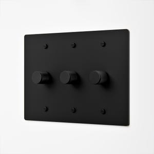 May include: A rectangular matte black wall plate featuring three circular, knurled control knobs arranged horizontally. The plate is secured to the wall with six matching black flathead screws, positioned in two rows of three at the top and bottom.