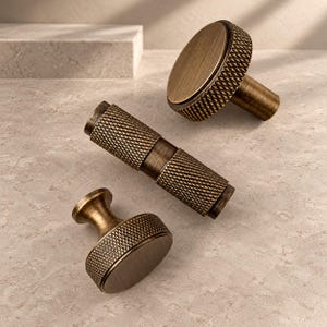 May include: Three pieces of antique brass hardware including two round knobs with a textured knurled edge and one cylindrical handle with a matching knurled pattern on both ends and a smooth center section, all featuring a brushed finish.