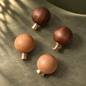 May include: Four spherical cabinet knobs featuring smooth wooden tops in two distinct shades of brown, paired with polished brass conical bases. Two knobs are crafted from dark walnut wood, while the other two are made from lighter wood.