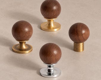 Op de afbeelding: Vier kastknoppen met bolvormige koppen van donkerbruin hout. Drie knoppen hebben metalen voetjes in verschillende afwerkingen, waaronder geborsteld messing, antiek messing en gepolijst chroom, terwijl één knop een cilindrische messing voet heeft.