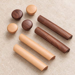 May include: A collection of wooden cabinet hardware including four round knobs and four cylindrical bar pulls. The items are crafted from two distinct wood tones, featuring a light natural finish and a darker, rich brown walnut-colored finish.
