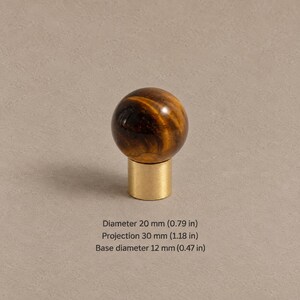 May include: A spherical tiger's eye stone knob set on a cylindrical brass base. The knob has a diameter of 0.79 inches, a projection of 1.18 inches, and a base diameter of 0.47 inches. The stone features brown and gold bands.