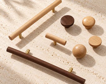 May include: A collection of wooden cabinet hardware including two long bar pulls, one short T-bar pull, and three round knobs. The hardware features light and dark wood finishes with gold-toned metal mounting posts for attachment to furniture.