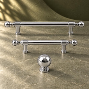 May include: A collection of three polished chrome cabinet hardware pieces consisting of two horizontal bar pulls with spherical end caps and one matching spherical knob, all featuring a smooth, reflective metallic finish.
