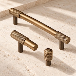 May include: A set of three brass-toned cabinet hardware pieces including one long bar pull, one T-shaped pull, and one cylindrical knob. Each piece features a textured, diamond-patterned knurled grip section and a smooth, brushed metal finish.