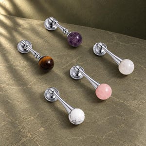 Peut inclure: Cinq poignées de placard en métal avec des extrémités en pierre sphérique. Les poignées présentent une quincaillerie argentée polie et des pierres rondes violettes, brunes, blanches, rose clair et blanches veinées de noir.