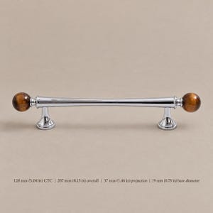 Peut inclure: Une poignée de meuble en chrome poli avec deux sphères en pierre œil-de-tigre marron aux extrémités. La quincaillerie mesure 128 mm d'entraxe, 207 mm de longueur totale, 37 mm de projection et 19 mm de diamètre de base.