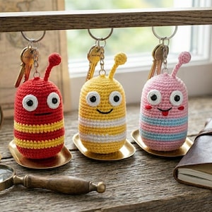 Peut inclure: Trois porte-clés crochetés à la main en forme de larves de dessins animés. Les porte-clés sont rouges, jaunes et roses, avec des yeux blancs et des visages souriants. Chaque porte-clés est attaché à un anneau métallique avec des clés.