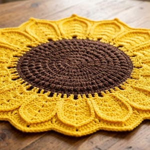 May include: A handmade crochet sunflower doily. The center is a dark brown, surrounded by yellow petals. The doily is placed on a wooden table. The sunflower design is a decorative item.