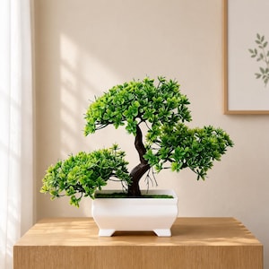 May include: An artificial bonsai tree with vibrant green leaves and a dark brown trunk, potted in a rectangular white ceramic container with four small feet. The plant features a layered canopy structure and is filled with green moss at the base.