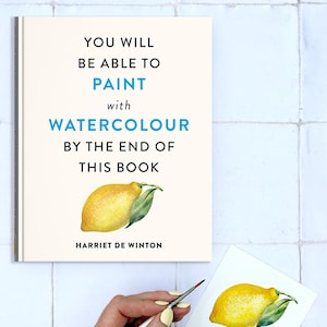 Peut inclure: Un livre intitulé "YOU WILL BE ABLE TO PAINT with WATERCOLOUR BY THE END OF THIS BOOK" de Harriet De Winton, avec une illustration de citron. Une main tient un pinceau au-dessus d'une aquarelle de citron et d'échantillons de couleurs.