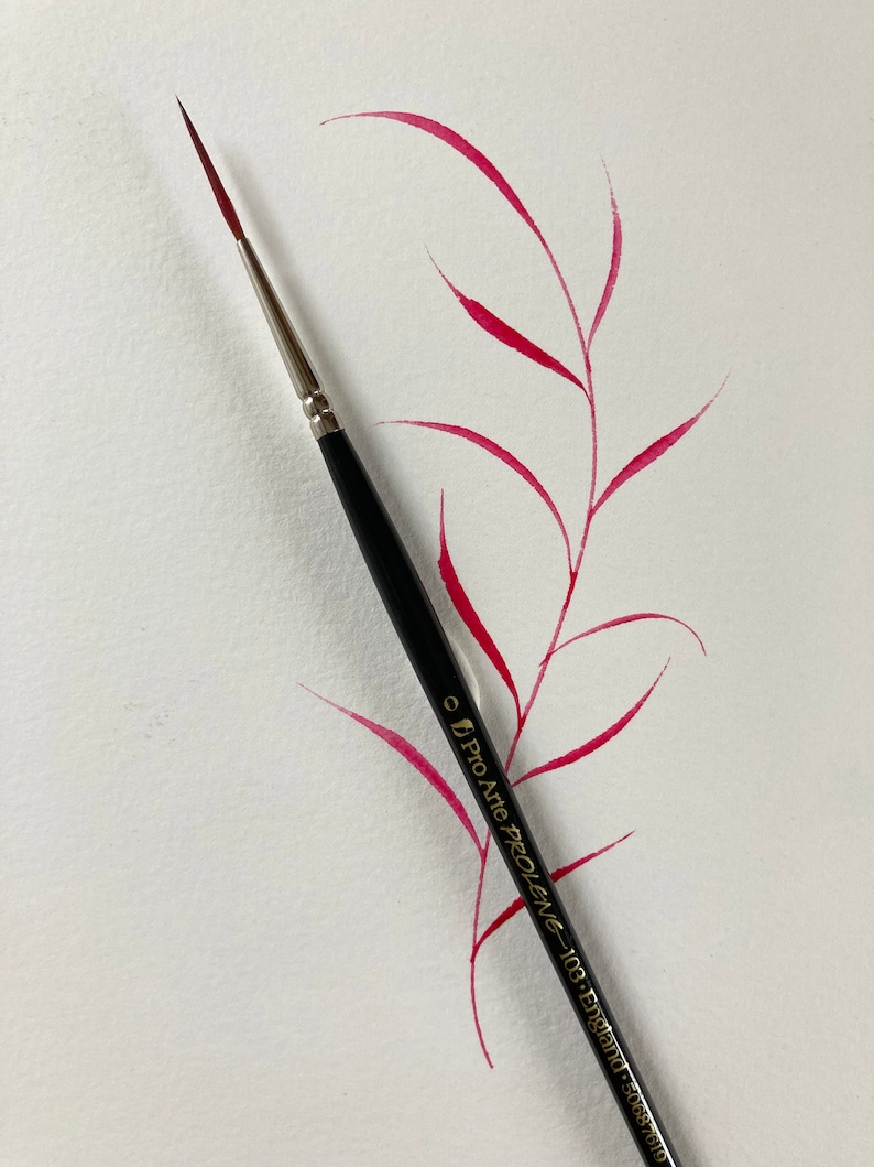 May include: A close-up of a black paintbrush with a red paint stroke on a white surface. The brush is labeled "Pro Arte Prolene - 10/8 - England - 5085/108".