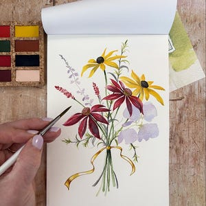 May include: A watercolor painting on paper depicting a floral bouquet with yellow coneflowers, deep red echinacea, light purple blossoms, and green foliage. The stems are tied together with a thin, golden yellow ribbon. A small paintbrush is visible.