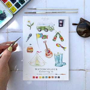 Peut inclure: Illustration à l'aquarelle avec des images d'une camionnette verte, d'une guitare, d'un microphone, d'un hamburger, d'une tente et de bottes. Les mots "WATERCOLOUR Colouring in" sont imprimés sur la page. Pinceaux, palette d'aquarelle et lunettes de soleil sont également présents.