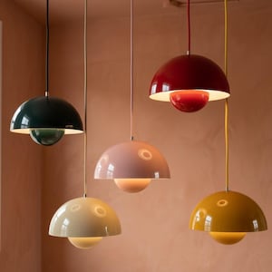 Puede incluir: Cinco lámparas colgantes de diferentes colores cuelgan del techo. Las pantallas son en forma de cúpula, con una lámpara esférica debajo. Los colores incluyen verde oscuro, rosa, rojo, crema y amarillo.